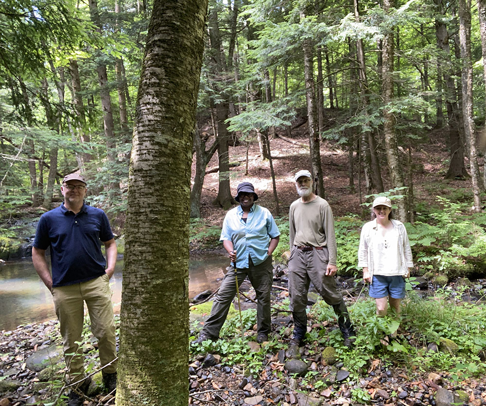 four people standing in the forest by a pool of water